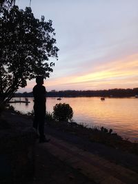 Silhouette man standing by lake against sky during sunset