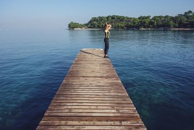 Man standing on pier over lake against sky