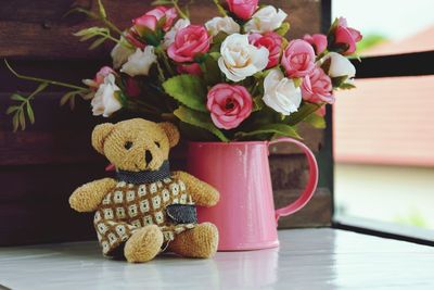 Close-up of teddy bear with roses in vase by window