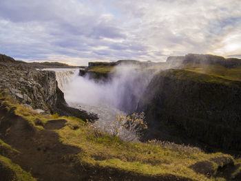 Scenic view of waterfall against cloudy sky