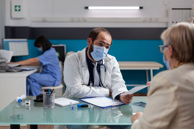 Doctor wearing mask prescribing medicine to patient