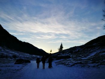 Silhouette people on snow covered landscape against sky