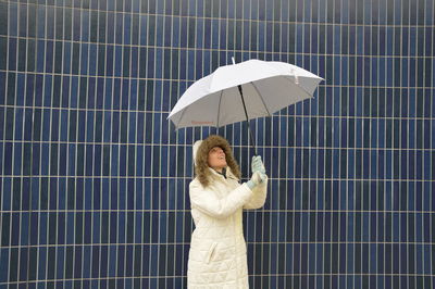 Woman with umbrella standing against wall