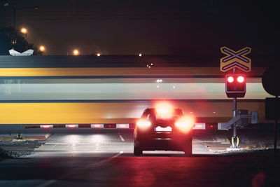 Railway at night. passenger train passing by railroad crossing while red warning lights stopped car