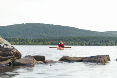 Rear view of man rowing in sea against clear sky