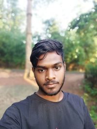 Portrait of young man standing against trees