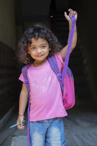 Portrait of cute smiling girl with backpack standing against black background