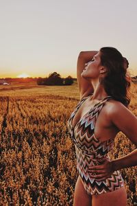 Seductive woman standing on field against sky during sunset