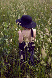 Child girl in a black hat and dress stands in a field with a grass in summer