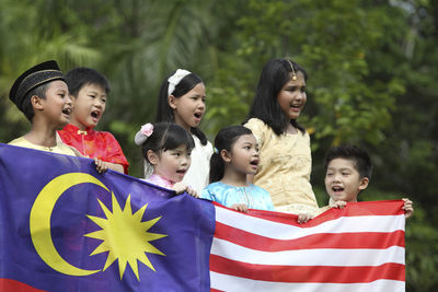 Friends holding malaysia flag while standing at park