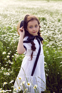 Portrait girl child in a white dress standing on a daisy field in a hat