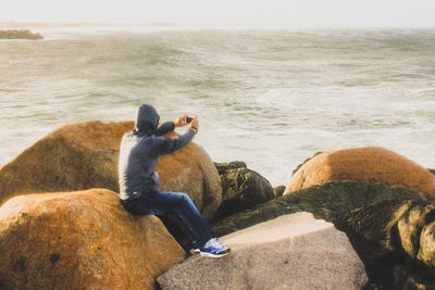 Rear view of man sitting on rock at beach