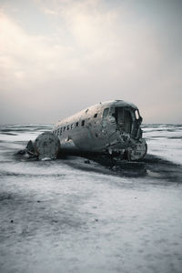 Abandoned boat on beach against sky during winter