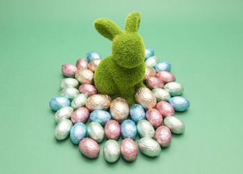 Green bunny, rabbit surrounded by small easter chocolate eggs, sweets wrapped in colorful bright