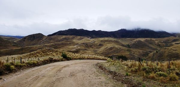 Dirt road leading towards mountains against sky