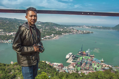 Portrait of man standing with camera against sea