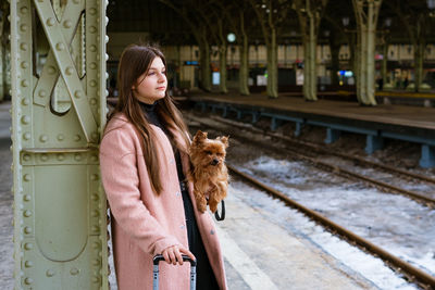 Woman traveler tourist walks with luggage and dog at train station in pink