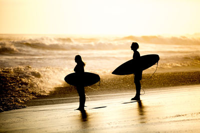 Silhouette people on beach against sky during sunset