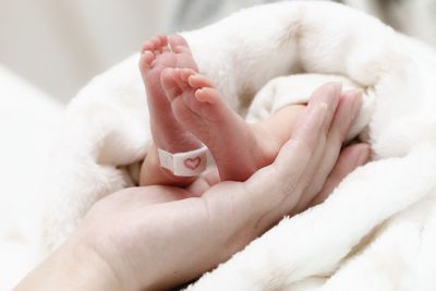 Cropped hand of mother holding baby feet on bed