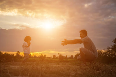 Father and son on field against sky during sunset