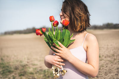 Young woman holding tulips while standing on field