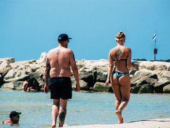 Rear view of friends on beach against clear sky