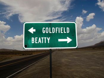 Green information sign by road against cloudy sky