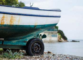 Close-up of boat moored on stoney beach against sky