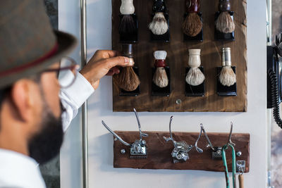 Crop stylish ethnic barber putting shaving tool on wall with different brushes in barbershop