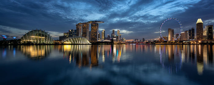 Illuminated modern cityscape by marina bay against sky