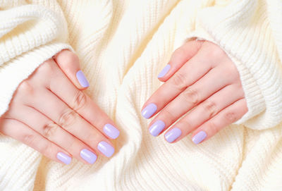 Female hands with violet manicure isolated on a white knitted background.