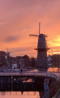 Transitional windmill in city against orange sky