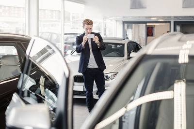 Man photographing car through smart phone at dealership store