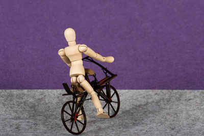 Wooden figurine on artificial bicycle against purple background