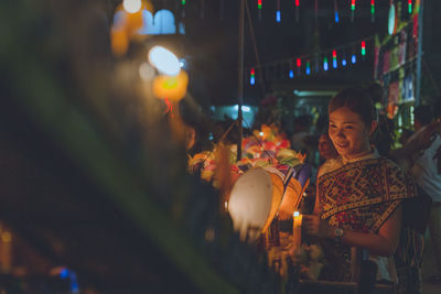 Smiling young woman standing at market at night