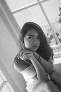 Portrait of young woman sitting by window at home