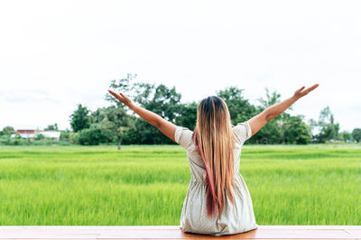 Rear view of woman with arms raised on field against sky