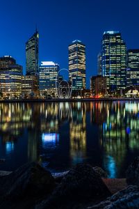 Illuminated buildings by river against sky in city at night