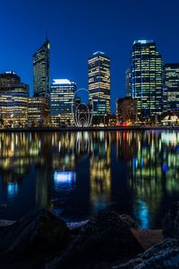 Illuminated buildings by river against sky in city at night