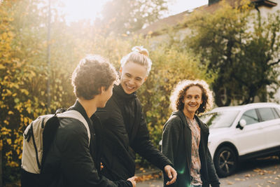 Smiling male friends talking while walking together on sunny day during autumn