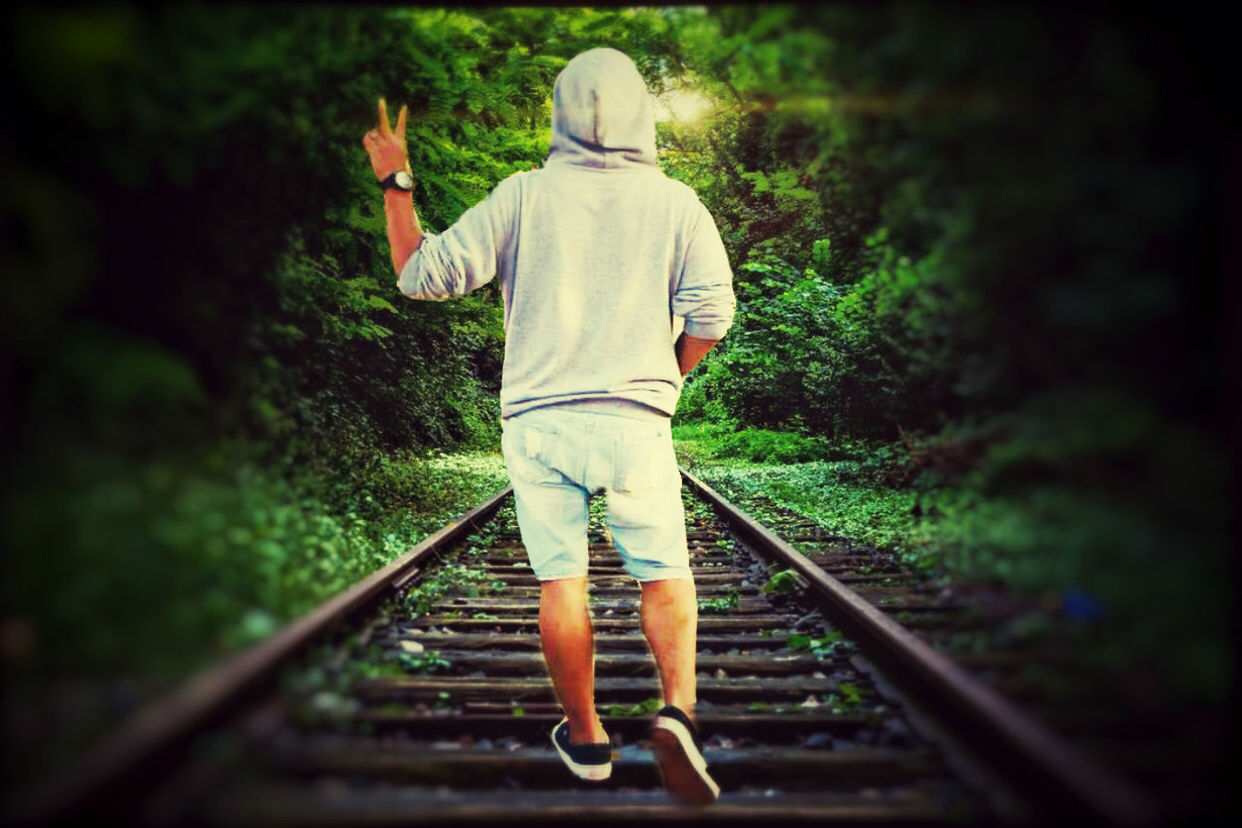 REAR VIEW OF MAN STANDING ON RAILROAD TRACKS