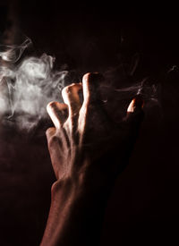 Midsection of person smoking cigarette against black background
