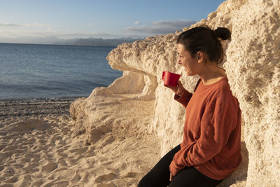 A woman with a cup in her hand at the beach of an island