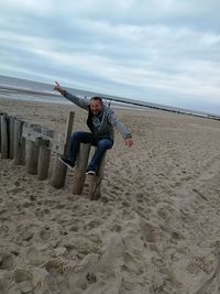 Portrait of young woman jumping on beach against sky