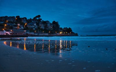 Illuminated buildings by sea against sky at night