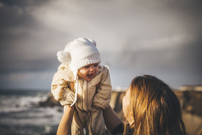 A woman is holding a baby near a lighthouse on the pacific coast