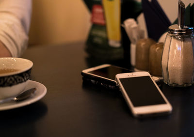 High angle view of smart phones by coffee cup on table