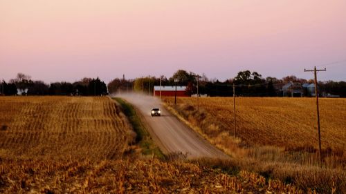 Illuminated car moving on road amidst agricultural field against sky during sunset