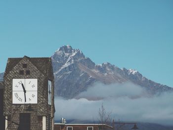 Low angle view of clock tower by rocky mountain against clear blue sky