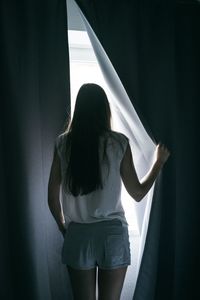 Rear view of woman standing against curtain